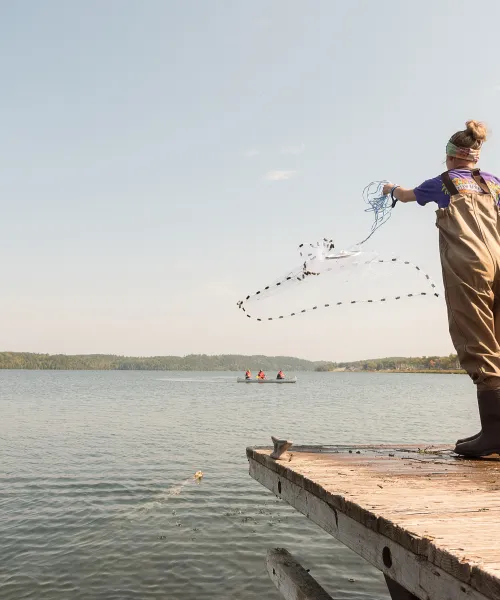 Student throwing fishing net into lake